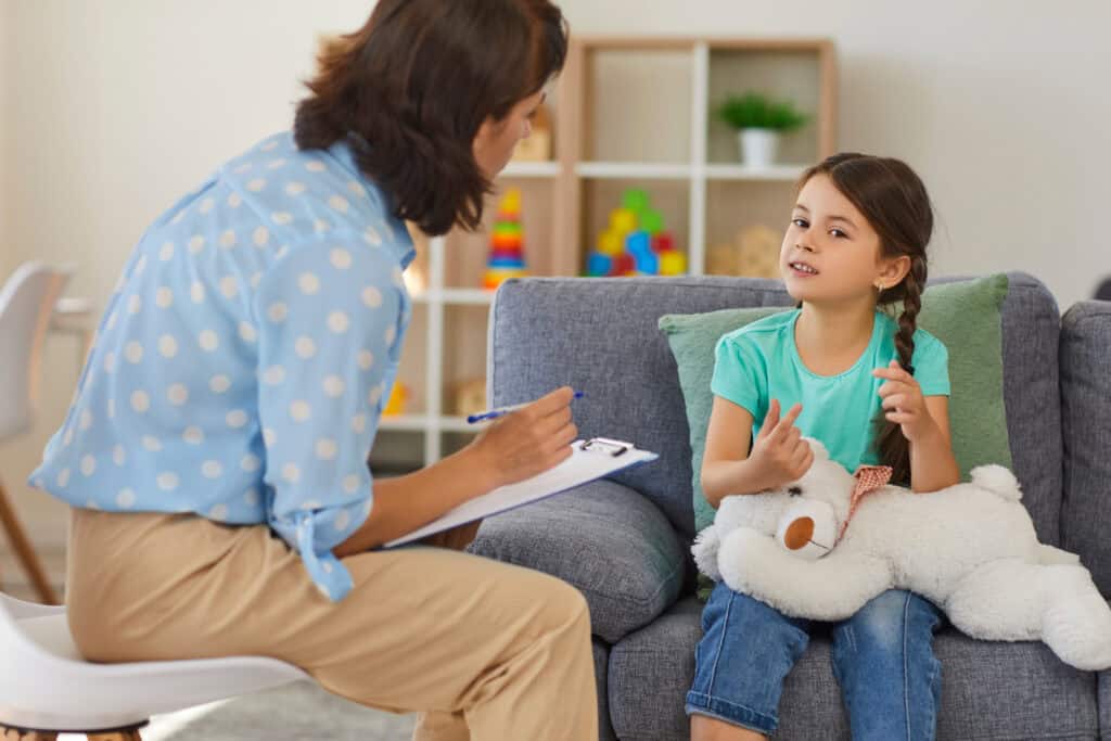 A social worker speaking with a young child and taking notes.