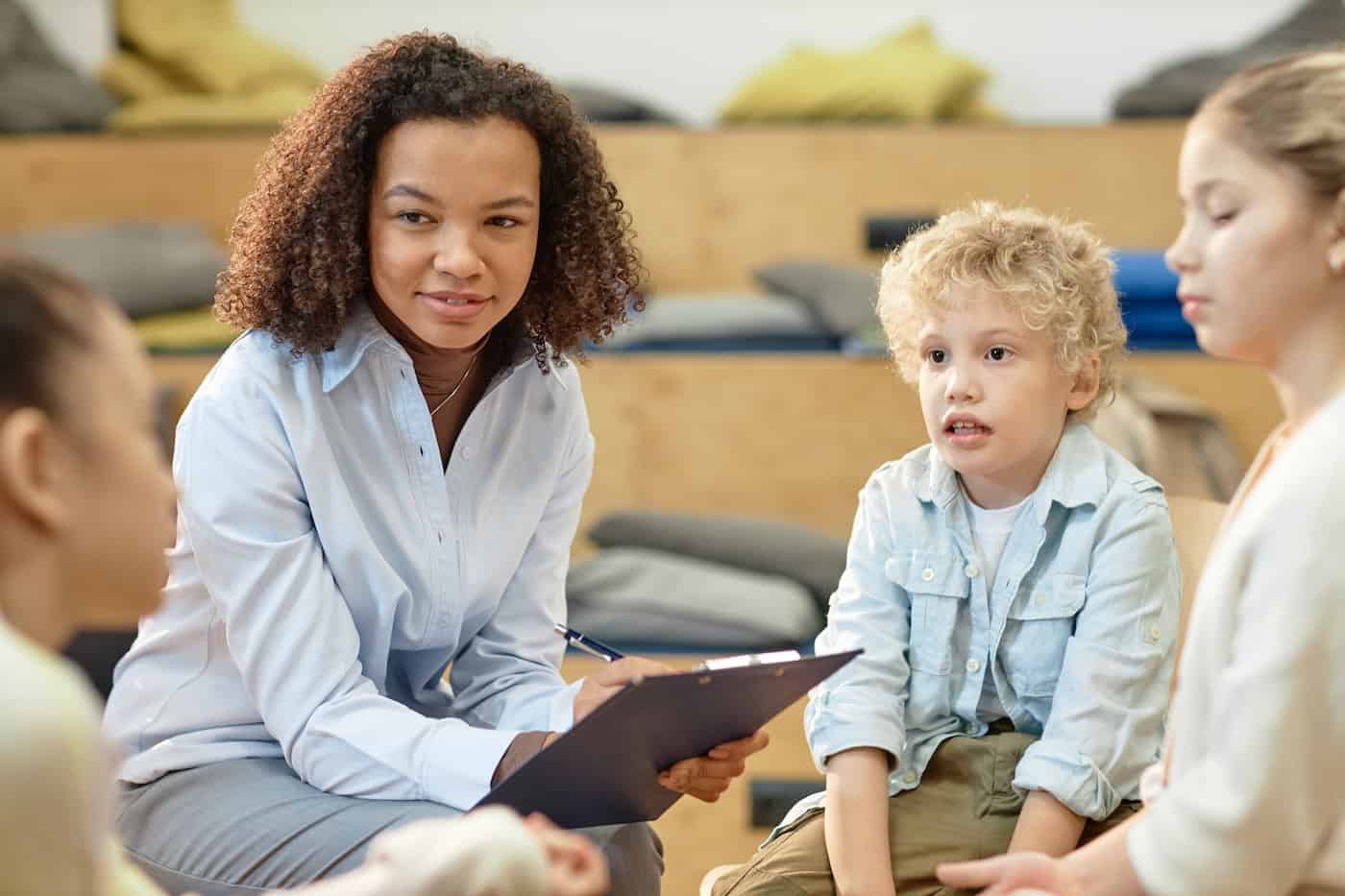 Portrait of smiling Black woman as female therapist listening to children in support group meeting at school