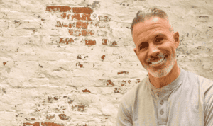 Dr. Aaron Burgess, Christian professor and business school faculty member at MVNU, smiling in front of a rustic white brick wall. An online learning expert dedicated to student success.