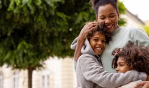 Smiling family of three standing outdoors together, representing support, happiness, and strong family bonds while pursuing online education.