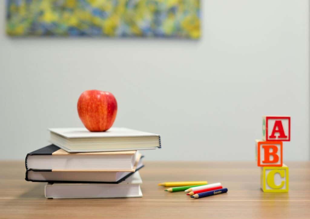 Stack of books with an apple, colored pencils, and alphabet blocks—symbolizing early education and MVNU’s online teaching degree in Columbus.
