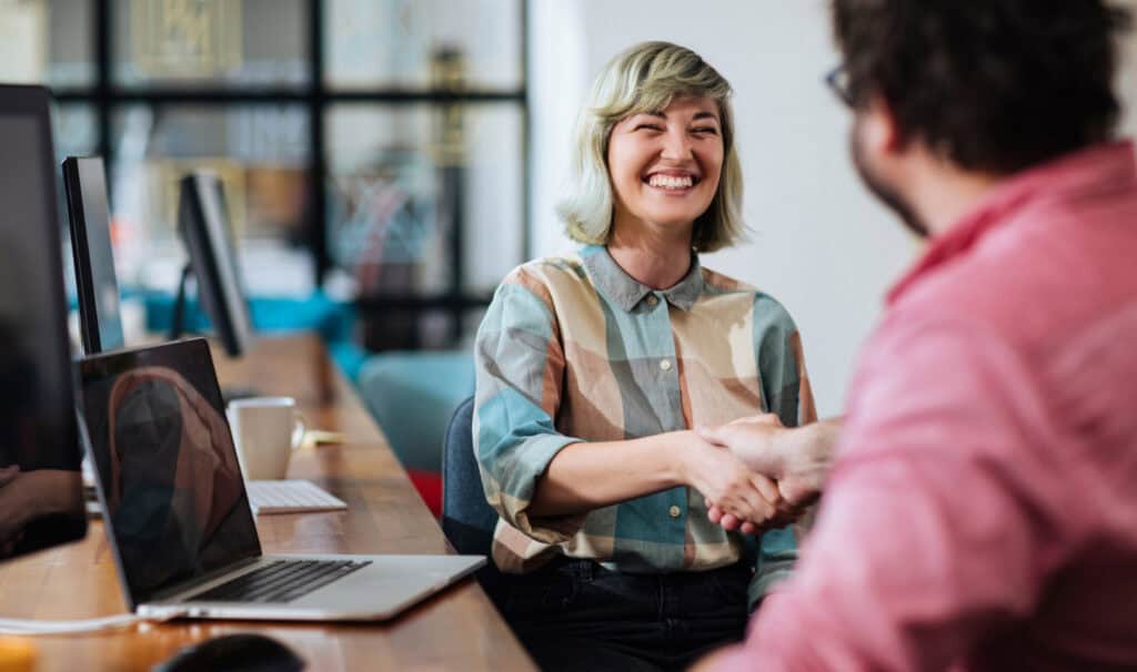 Smiling adult woman shaking hands with a colleague in a modern office, advancing her career through an online degree from MVNU while balancing work and education.