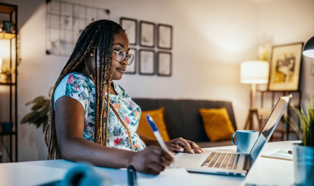 Adult female student taking notes while learning online at home